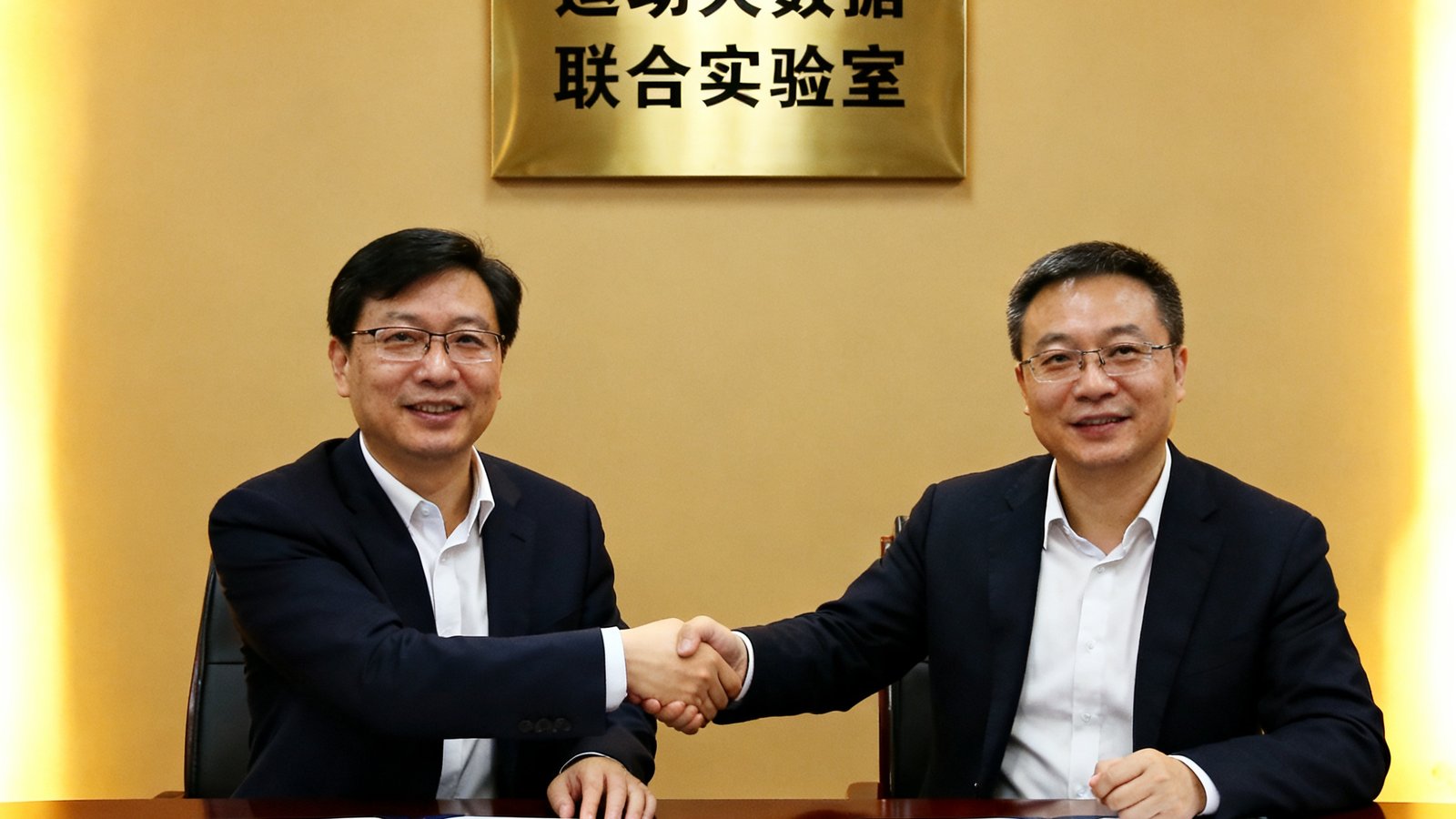 熊猫体育与电子科技大学签约仪式现场，双方代表在合作协议上签字握手，背后展示着运动大数据联合实验室的牌匾